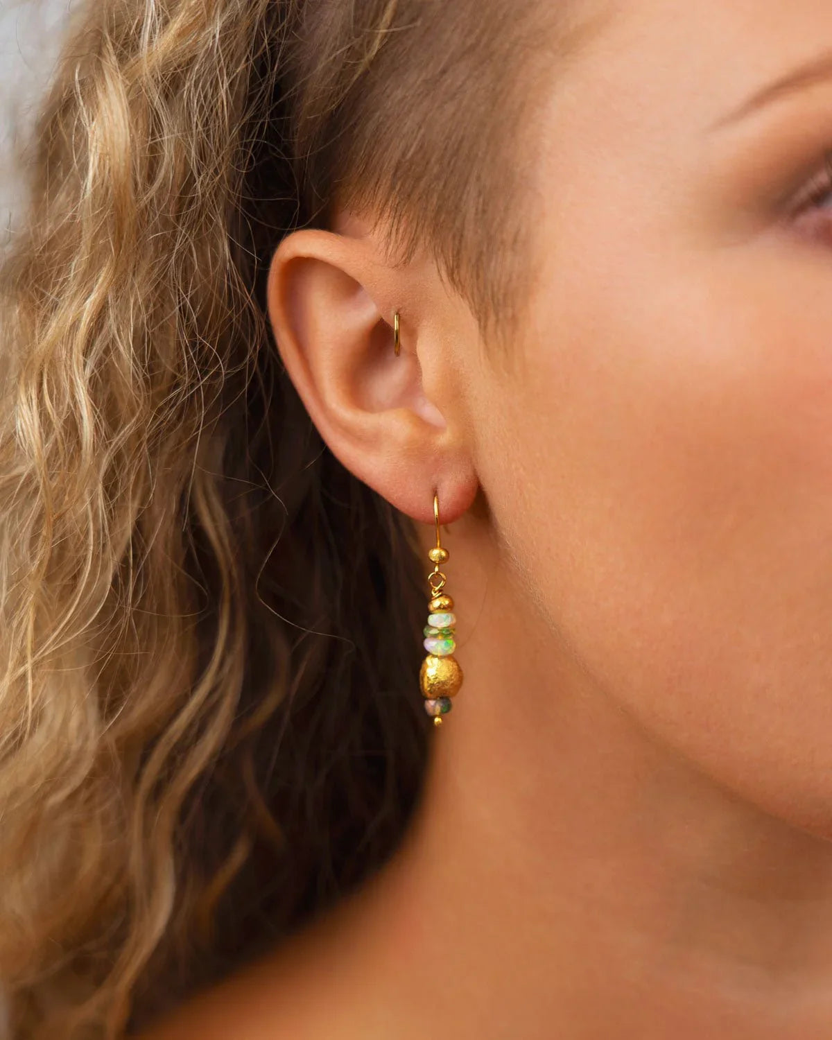 Dangly gold earrings with opal beads on ear, featuring organic shapes and earthy textures