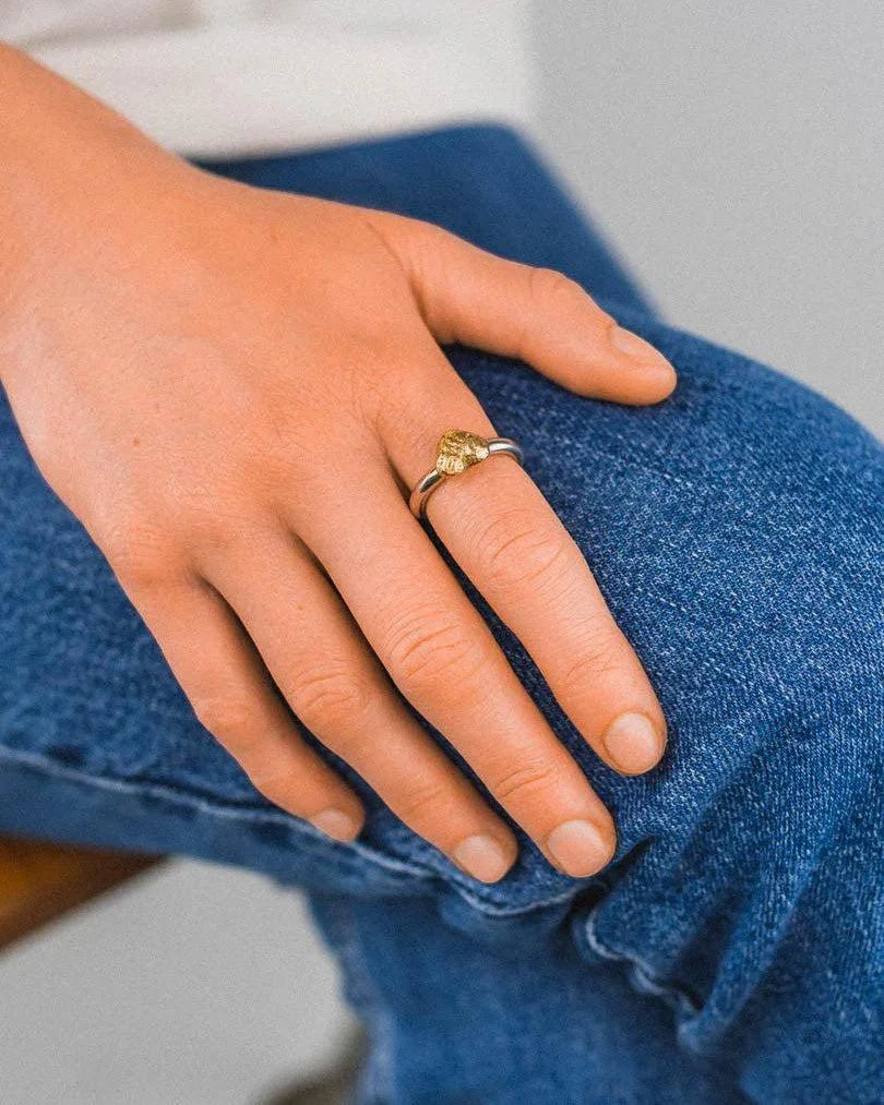 Silver band ring with a textured gold nugget heart being worn on a hand.