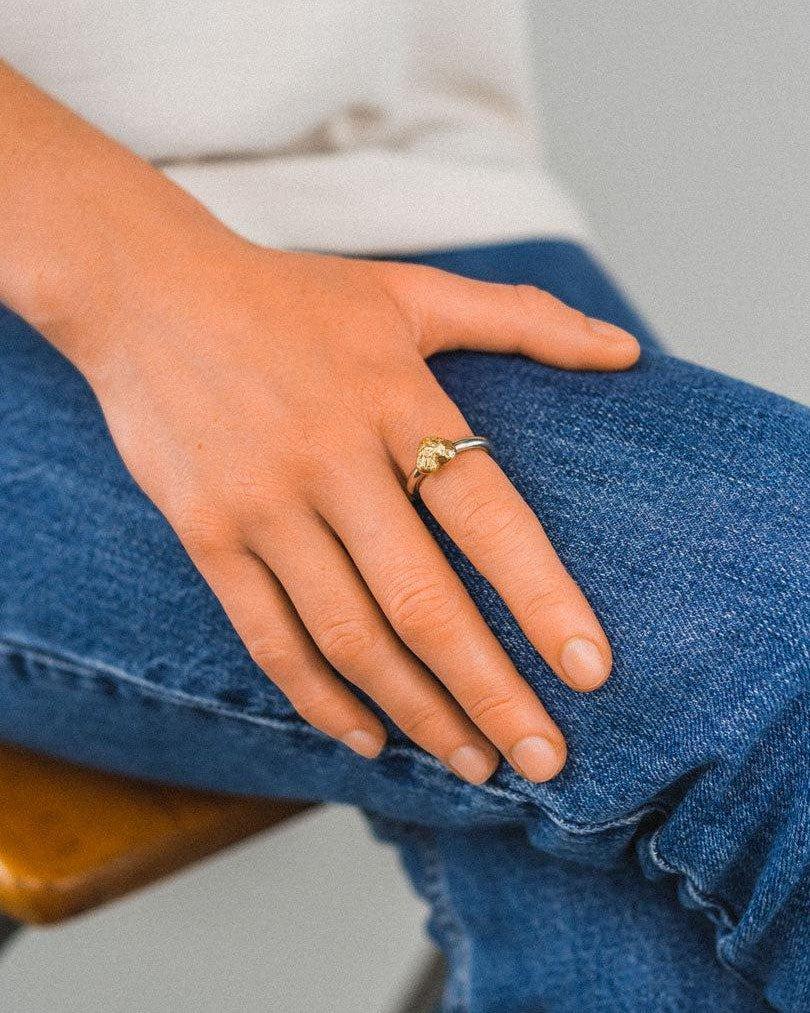 A silver band ring with a textured gold nugget heart worn on a person's finger.