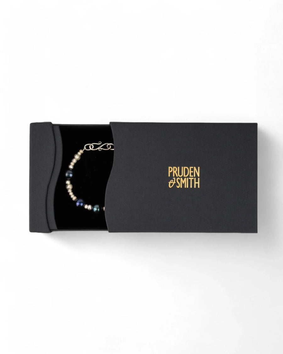 Silver and black pearl beaded bracelet displayed in a black gift box on white background