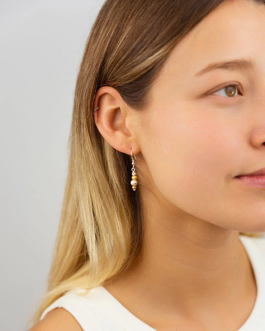 Woman wearing handcrafted silver and gold drop earrings with organic textured beads