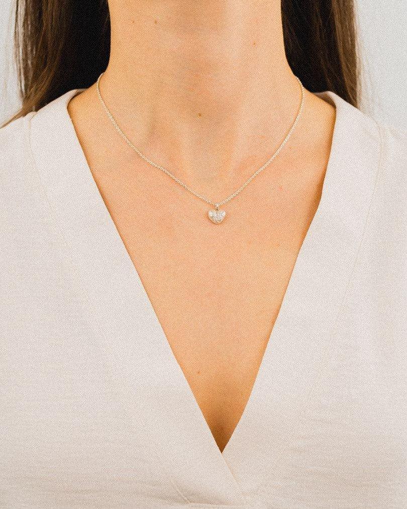 Delicate silver heart pendant necklace with organic texture on woman wearing a v-neck top