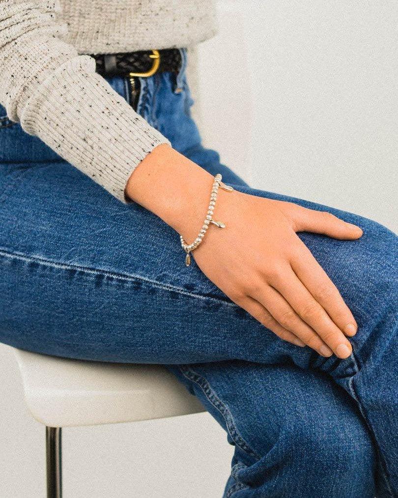 Silver teardrop charm bracelet with organic beads on wrist, worn with casual denim jeans