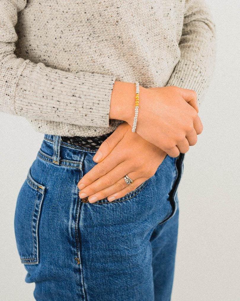 Silver bracelet with gold accent worn on wrist, paired with casual sweater and jeans.