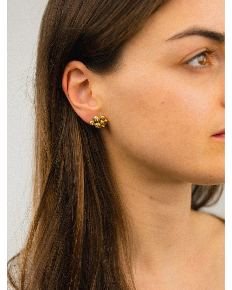 Woman wearing gold cluster stud earrings with ruby, emerald, sapphire, and diamond stones