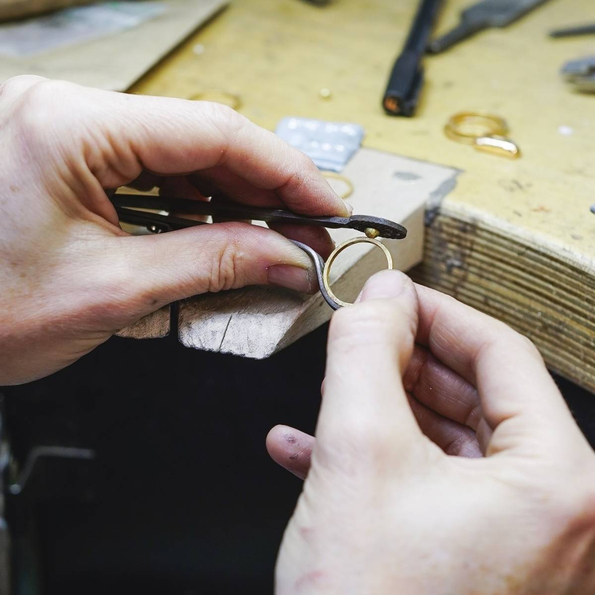 Close-up of hands working on a small metal object with tools in the background