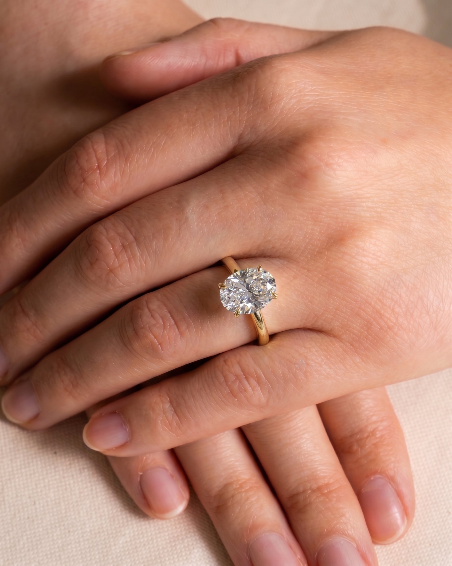yellow Gold oval solitaire engagement ring with a large diamond on a hand.
