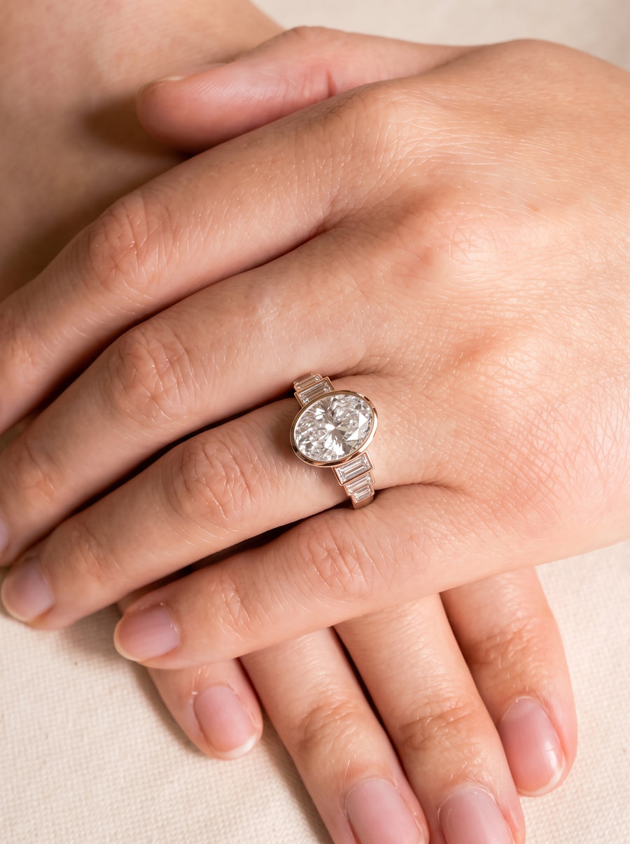 Oval diamond engagement ring in rose gold with baguette side stones worn on a finger.