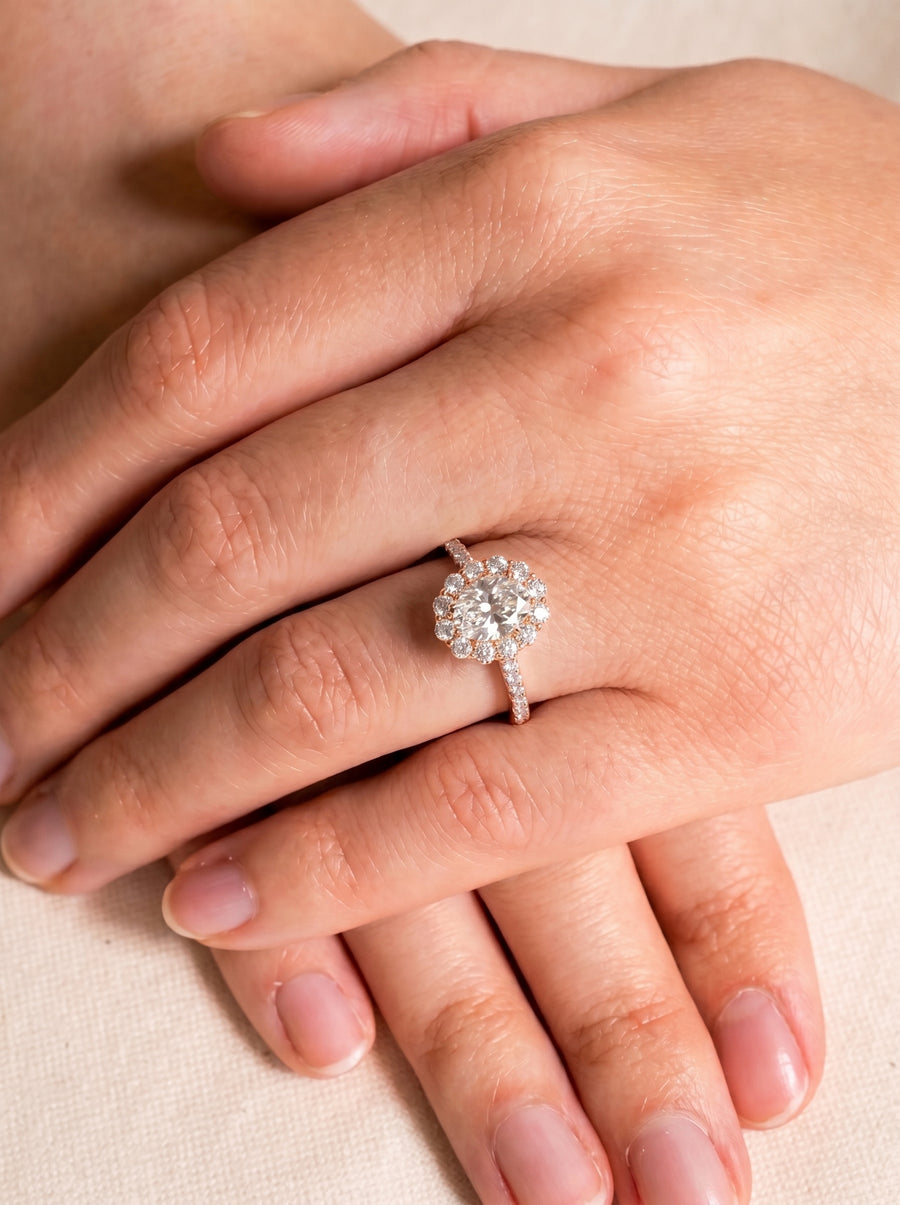 Oval cut diamond ring with a halo setting in rose gold worn on a finger.