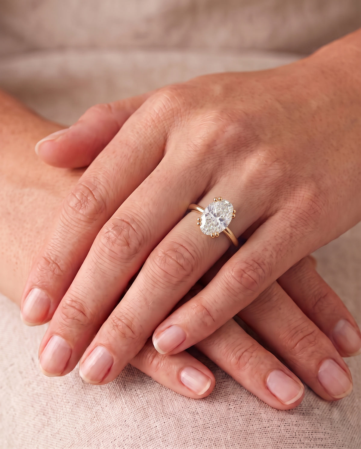 Oval cut diamond engagement ring with a hidden halo on a yellow gold band worn on a finger.