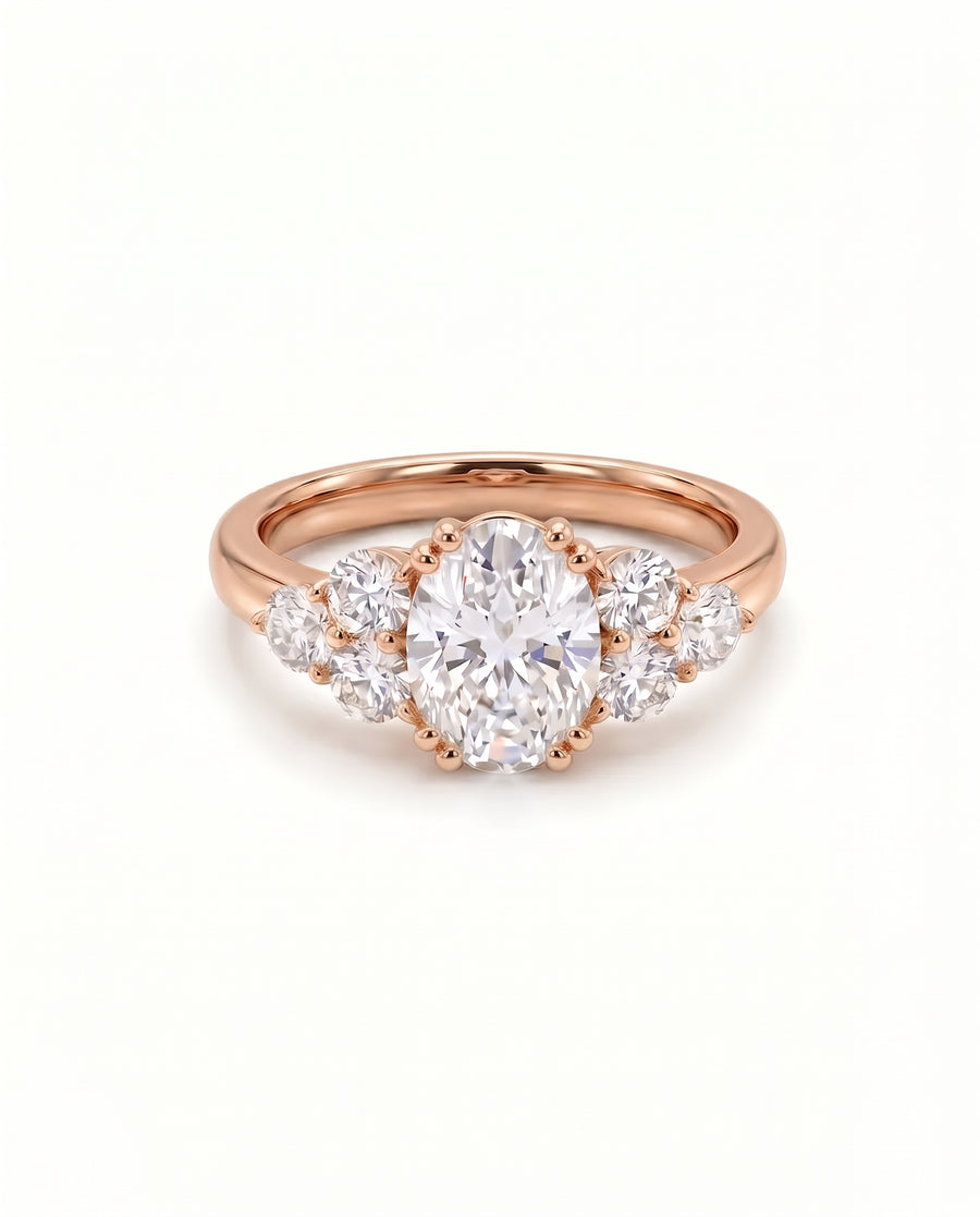 Oval cut diamond engagement ring with side stones in a rose gold trefoil claw setting.