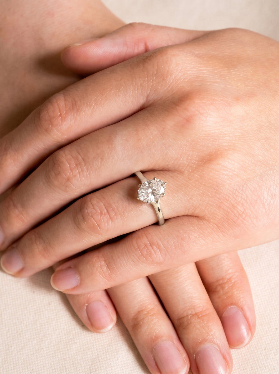 Oval cut diamond engagement ring in a silver-toned tulip claw setting worn on a finger.