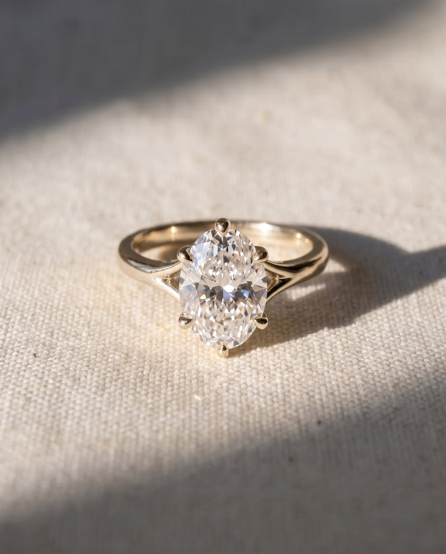 Oval cut diamond engagement ring in a gold tulip claw setting on a textured fabric background.