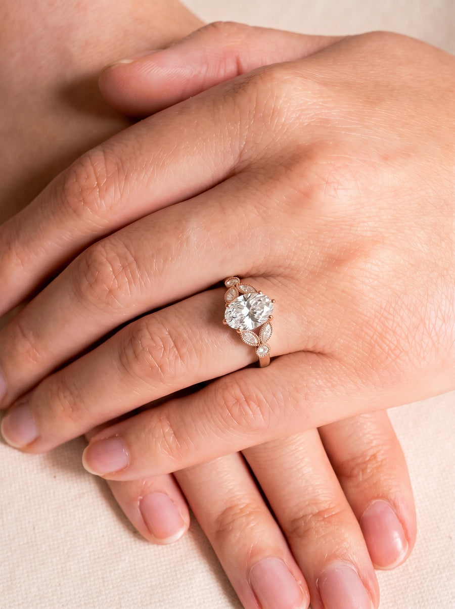 Oval cut diamond engagement ring in rose gold with marquise and round accent stones on a finger.