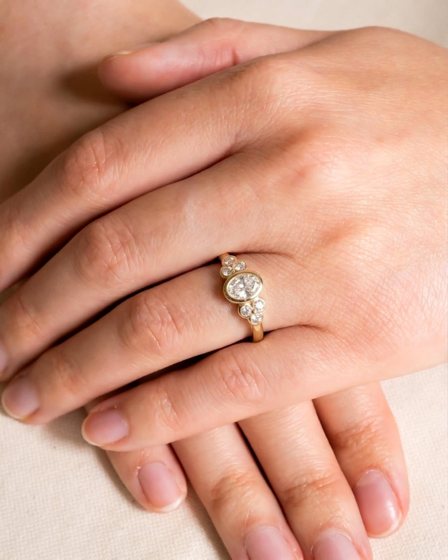 Gold oval trefoil engagement ring with multiple diamonds on a hand.