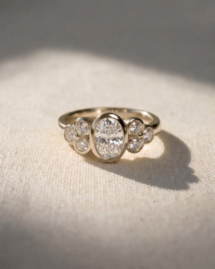 Oval diamond engagement ring in gold with a trefoil cluster of smaller round diamonds on each side.
