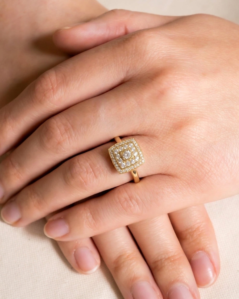 Gold cluster engagement ring with square diamonds on a hand.