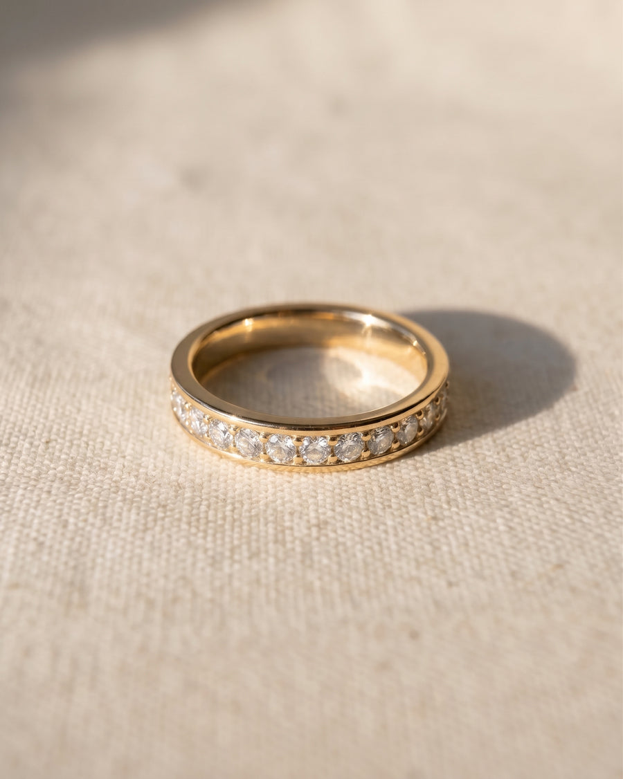 Gold ring with pavé diamonds on a light fabric surface.