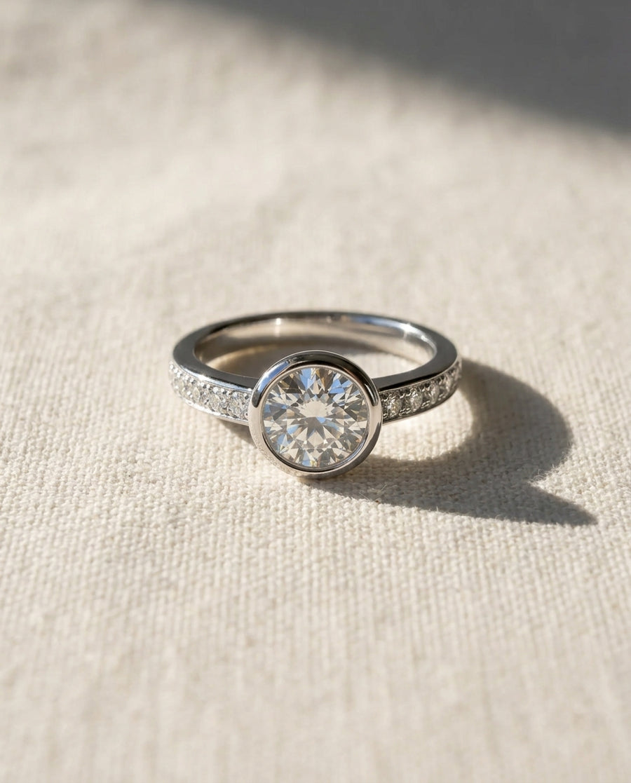 White gold pavé rub over diamond engagement ring on a light fabric surface.