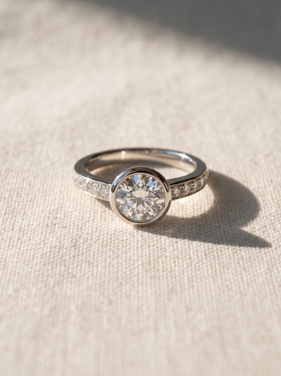 Silver engagement ring with a round diamond in a rub over setting and pavé set diamonds on the band.