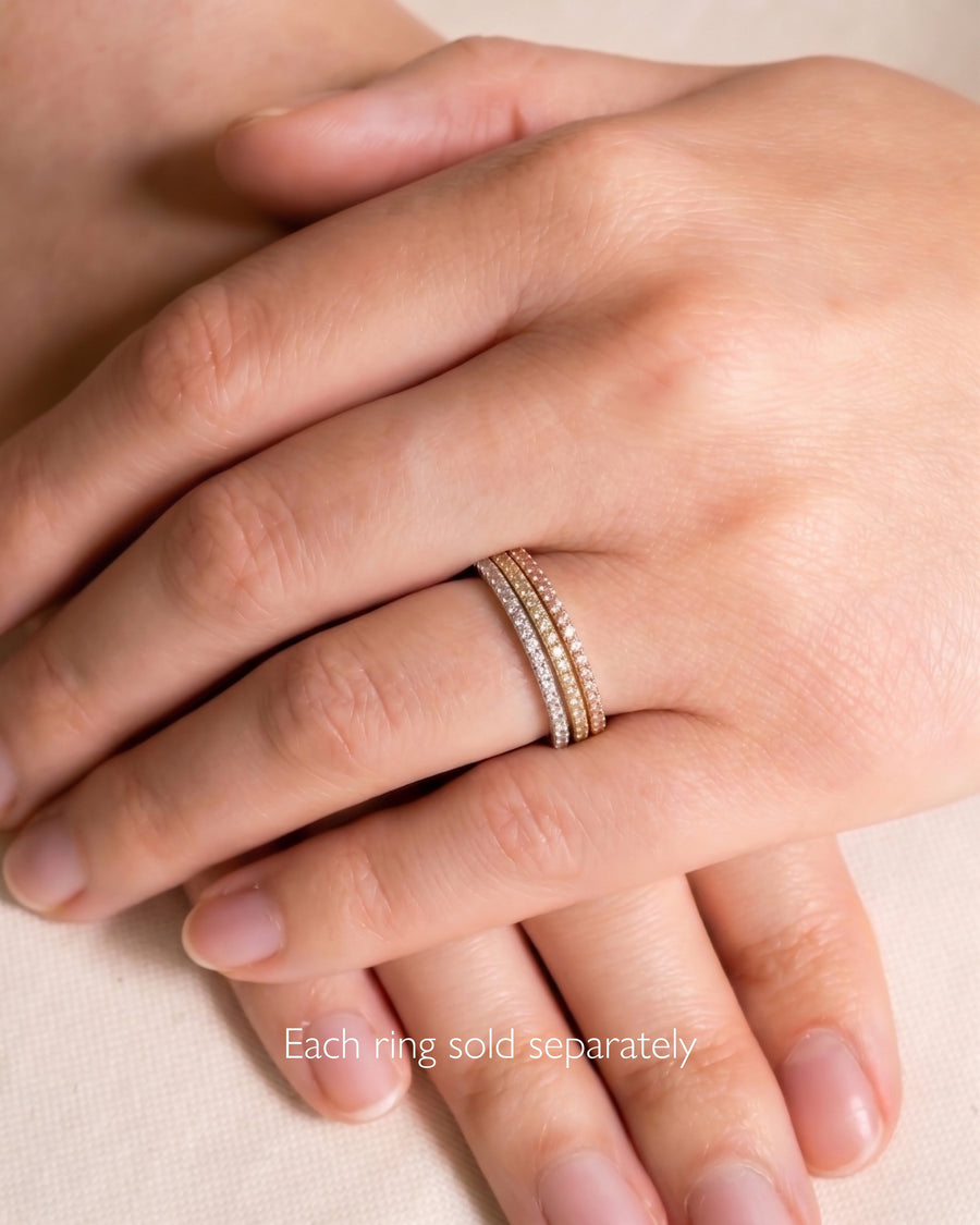 Slim pavé set diamond rings in rose, yellow, and white gold on a hand.