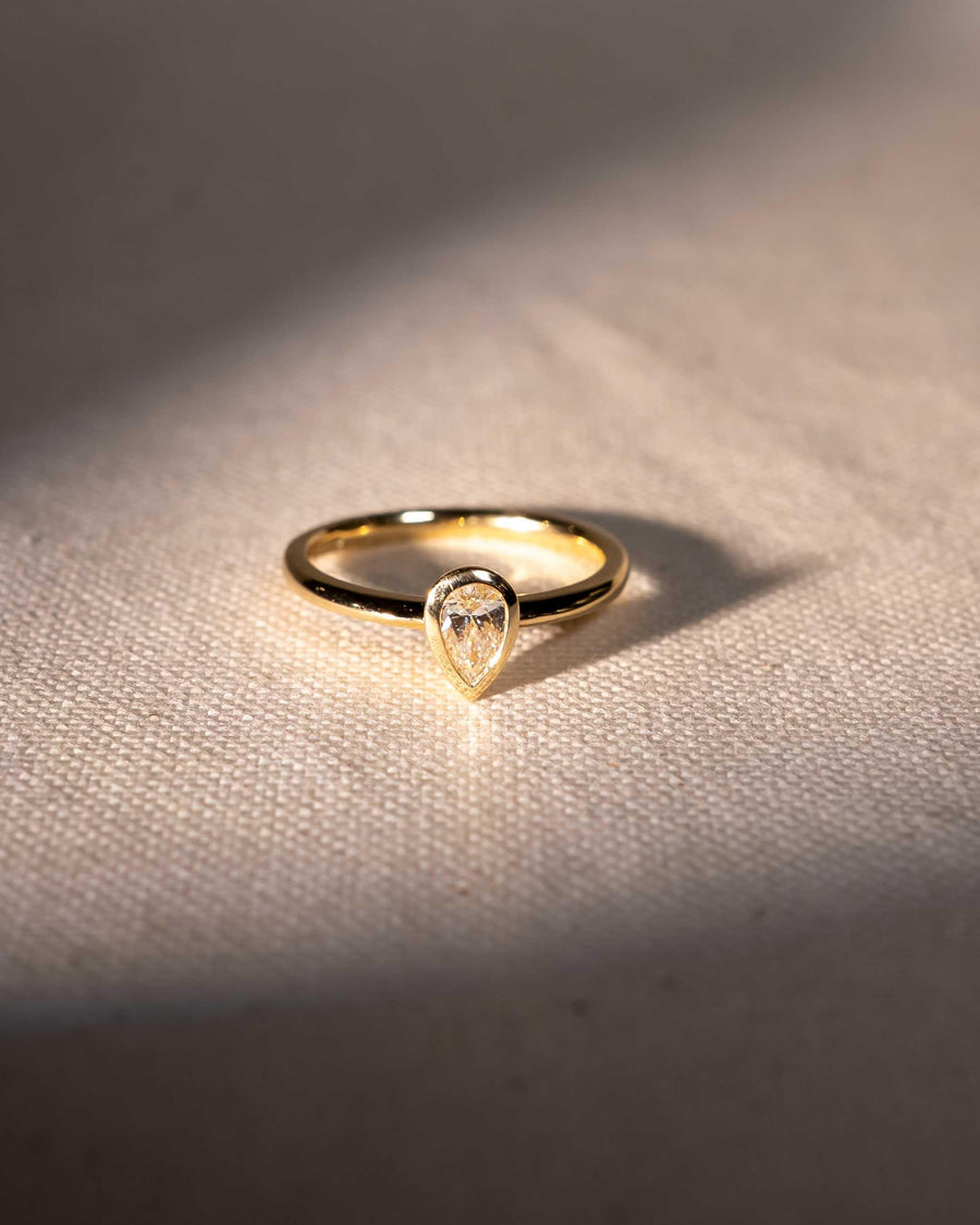 Yellow gold ring with a pear cut natural diamond in a bezel setting.
