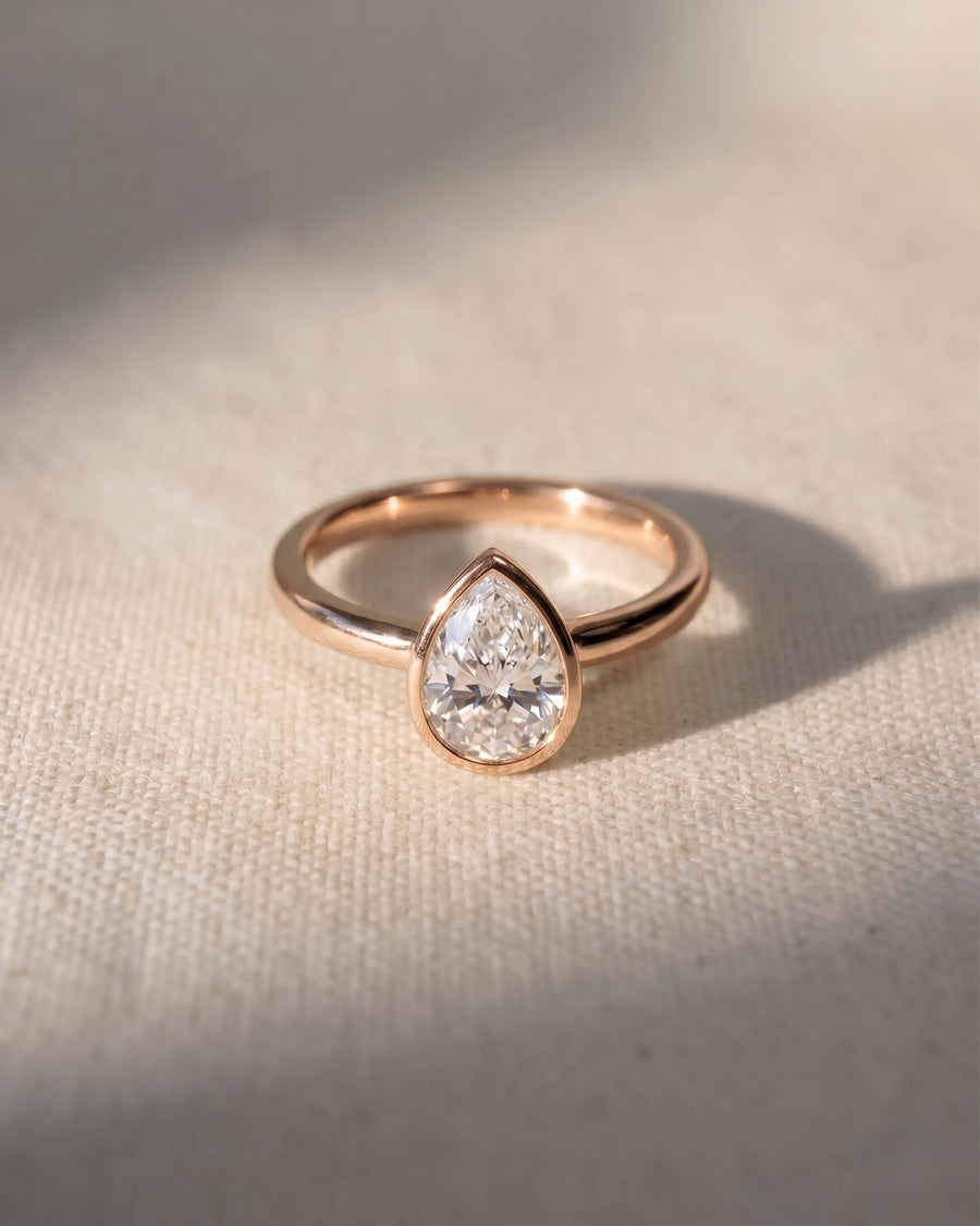 Rose gold engagement ring with a pear cut natural diamond in a bezel setting.