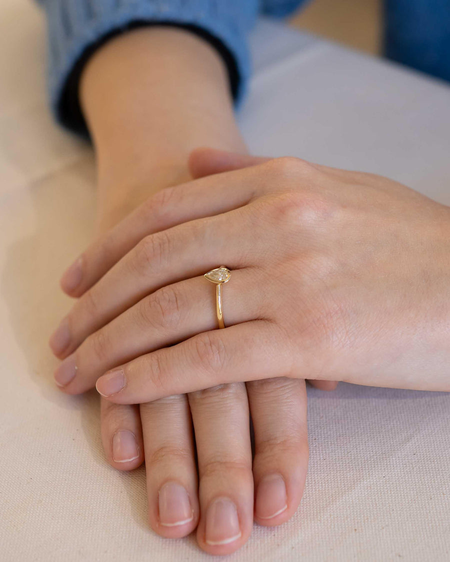Yellow gold ring with a pear cut natural diamond bezel setting on a hand.