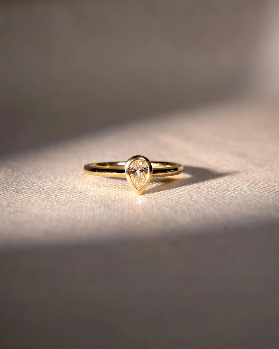 Gold ring with a pear-cut natural diamond in a bezel setting.