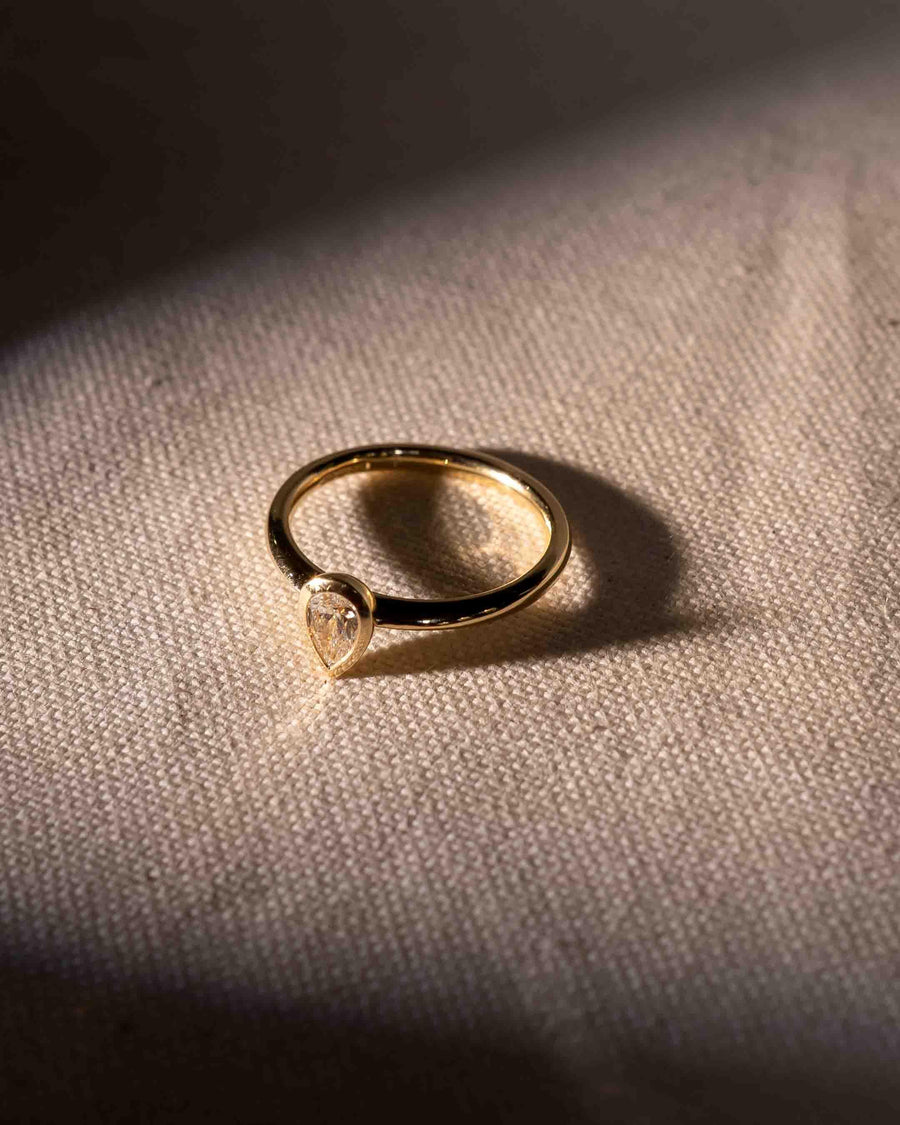 Gold ring with a pear-cut diamond in a bezel setting.