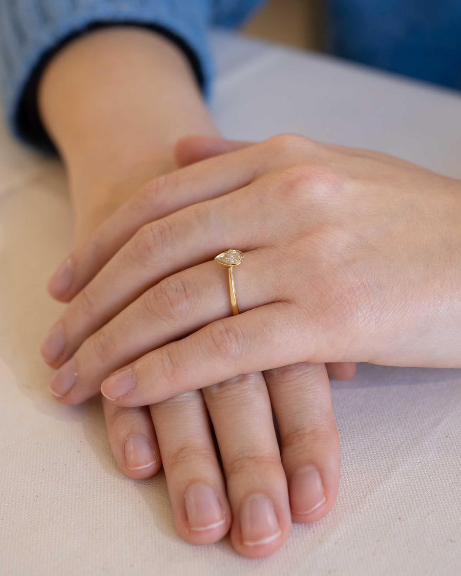 Yellow gold engagement ring with a pear cut diamond in a bezel setting.