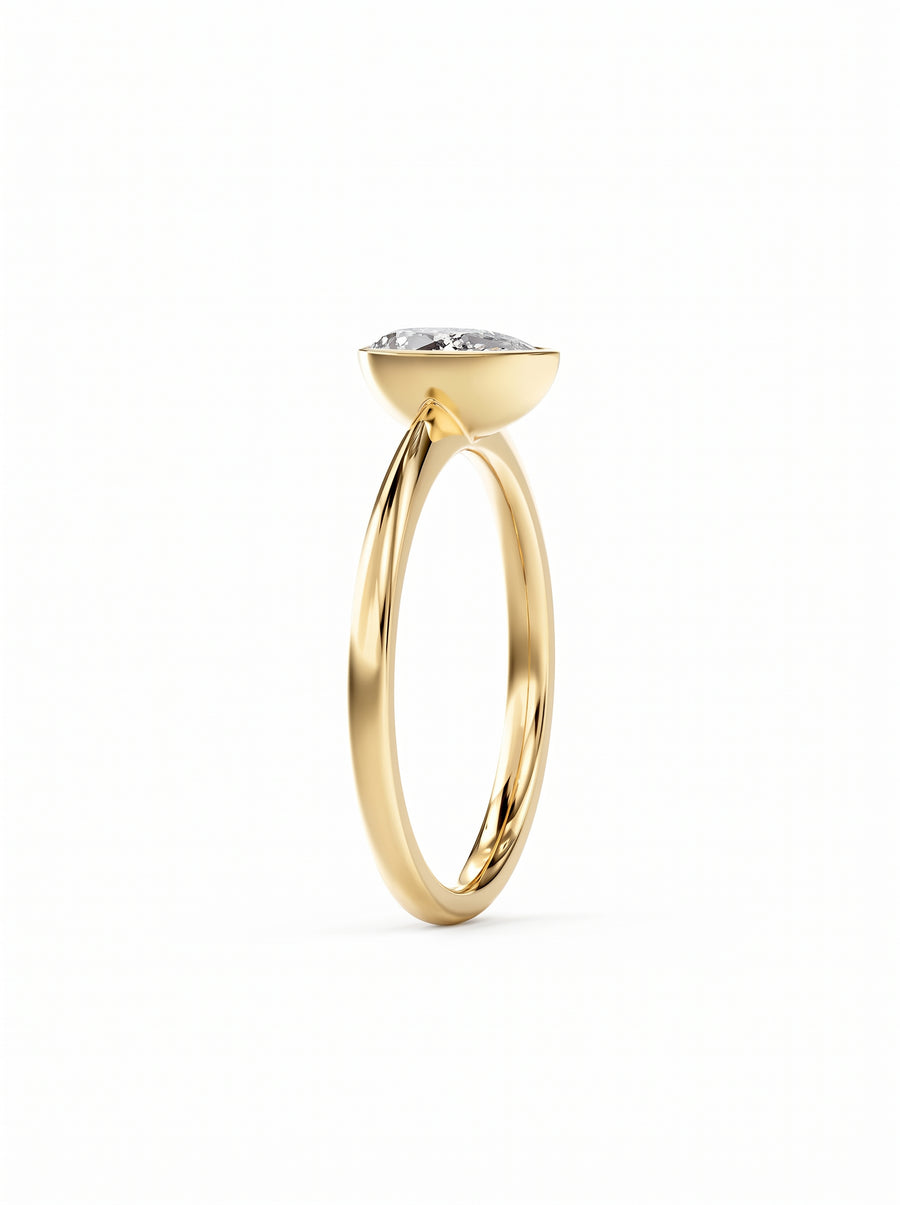 Pear cut diamond engagement ring in a gold bezel setting on a white background.