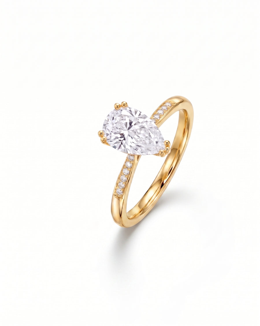 Gold engagement ring with a pear cut diamond and pavé band.