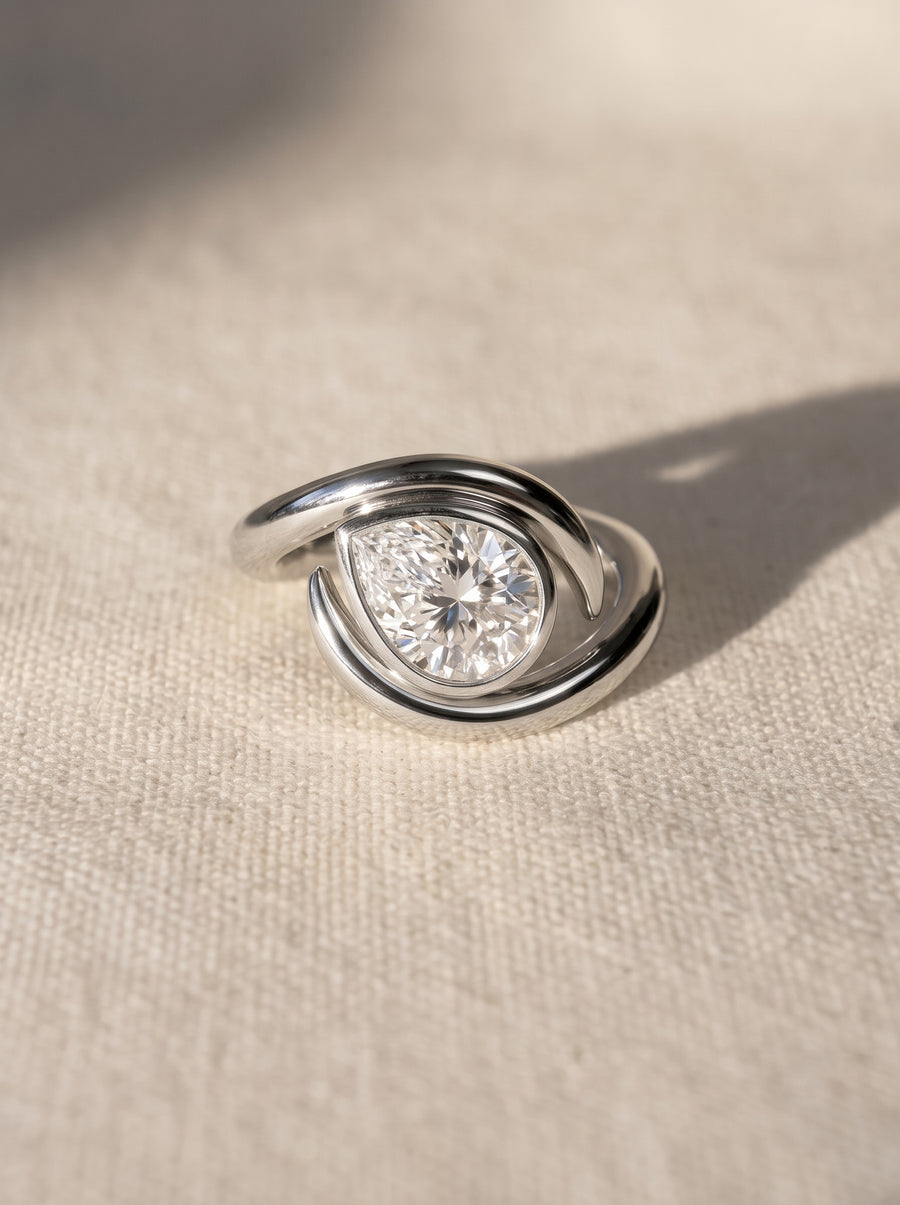 Pear cut diamond engagement ring in a silver-toned metal setting with a modern, swirling wrap design.