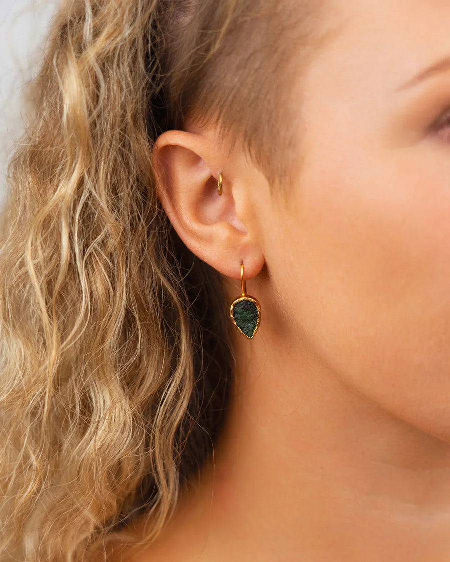 Woman wearing pear-shaped rough emerald drop earrings with gold settings