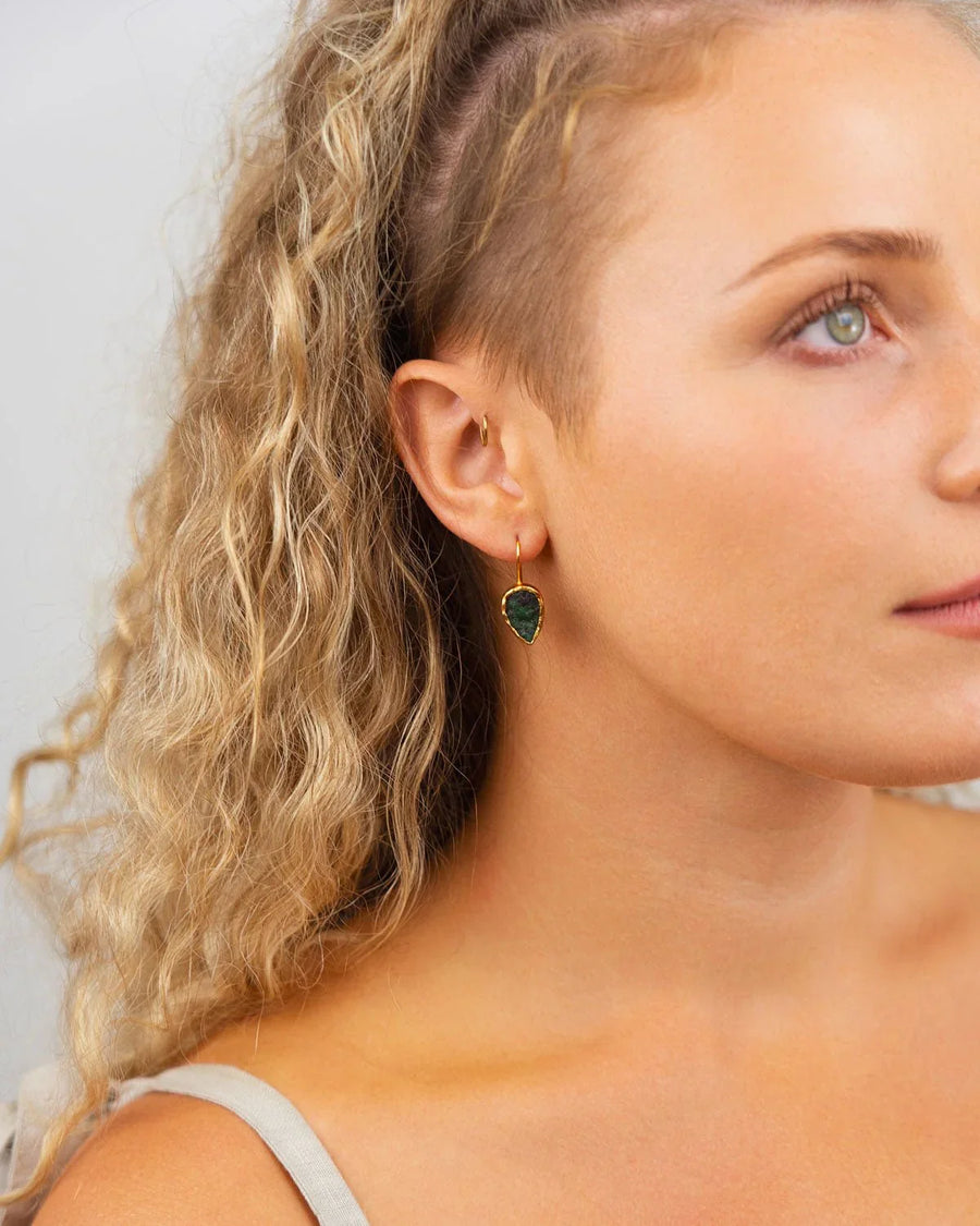 Woman wearing pear-shaped rough emerald drop earring set in gold