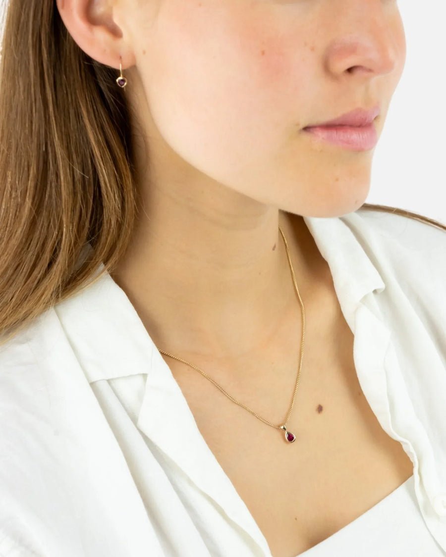 Woman wearing a gold chain necklace with pear-shaped ruby pendant and matching earring