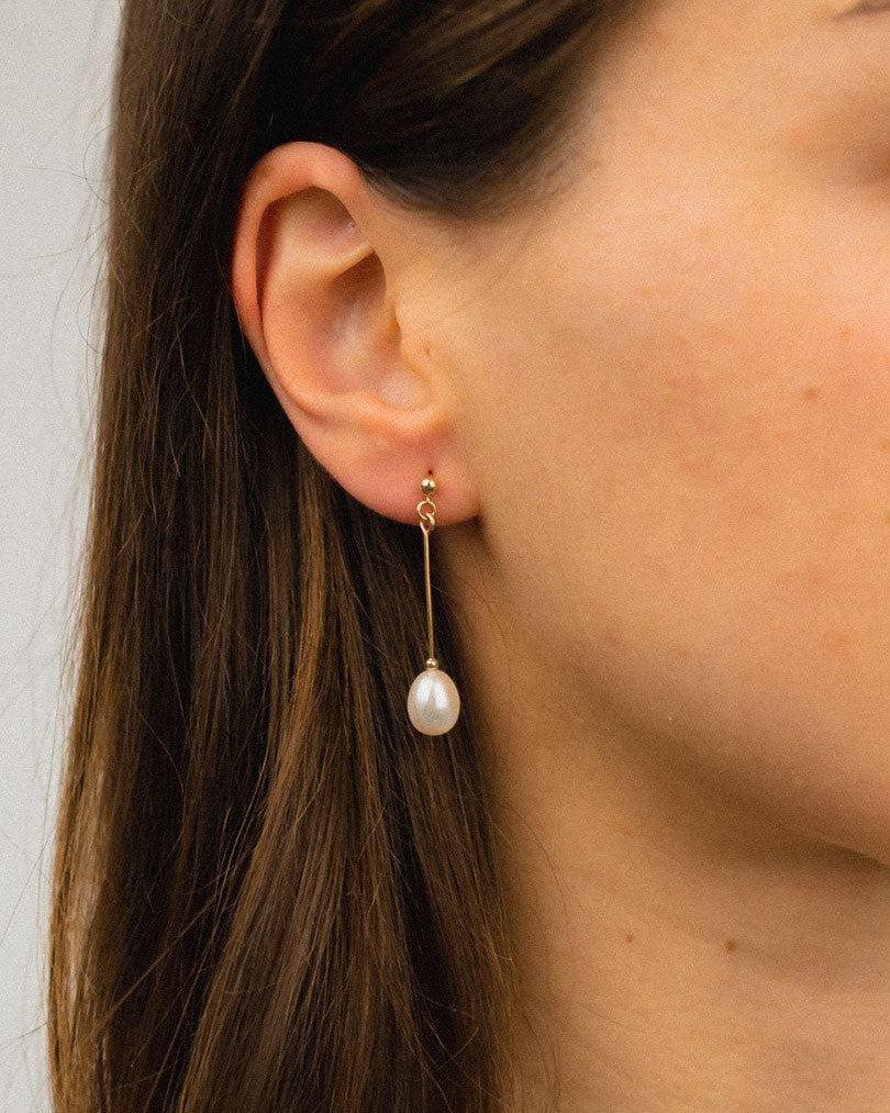 Gold bar drop earring with a single white pearl on model's ear