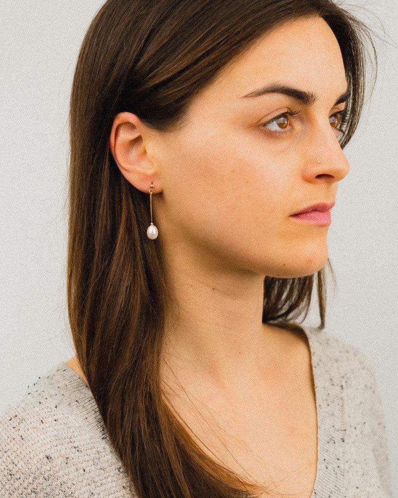 Woman wearing elegant pearl drop dangle earring in gold, side profile view