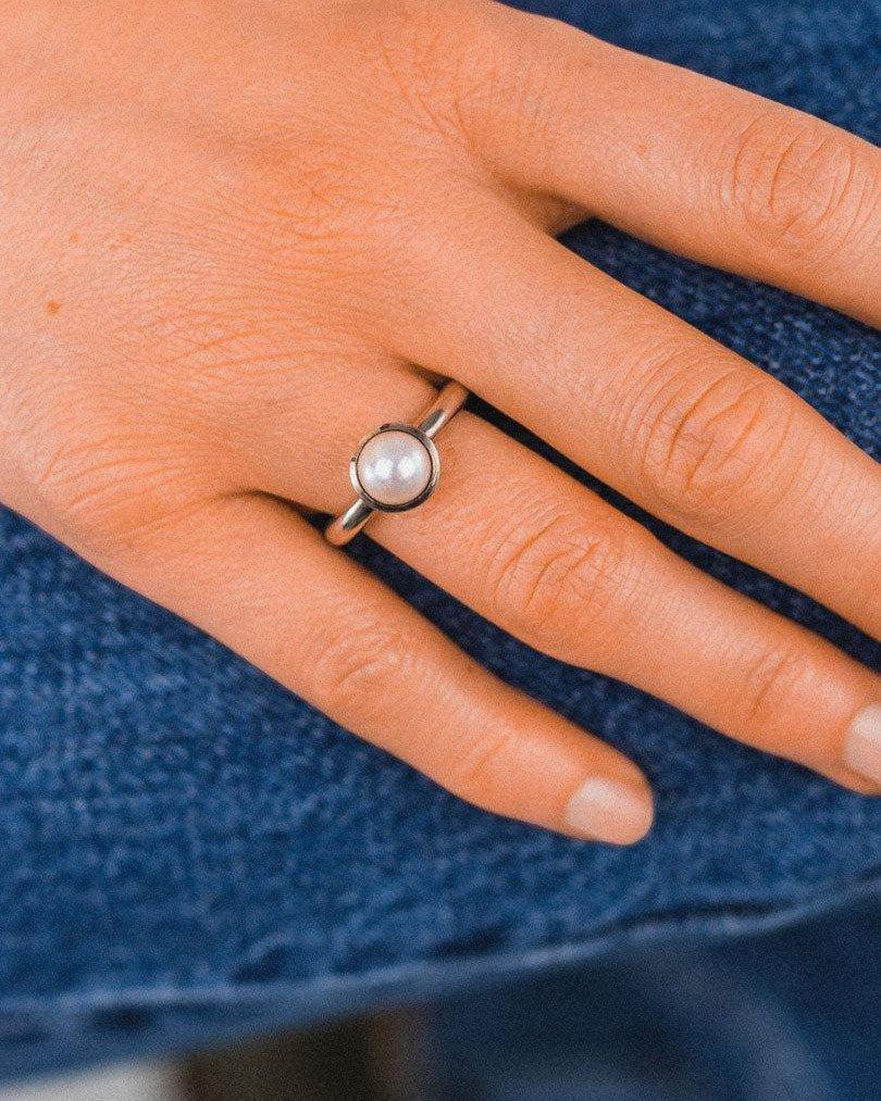 Silver ring with a single round white pearl on a hand.