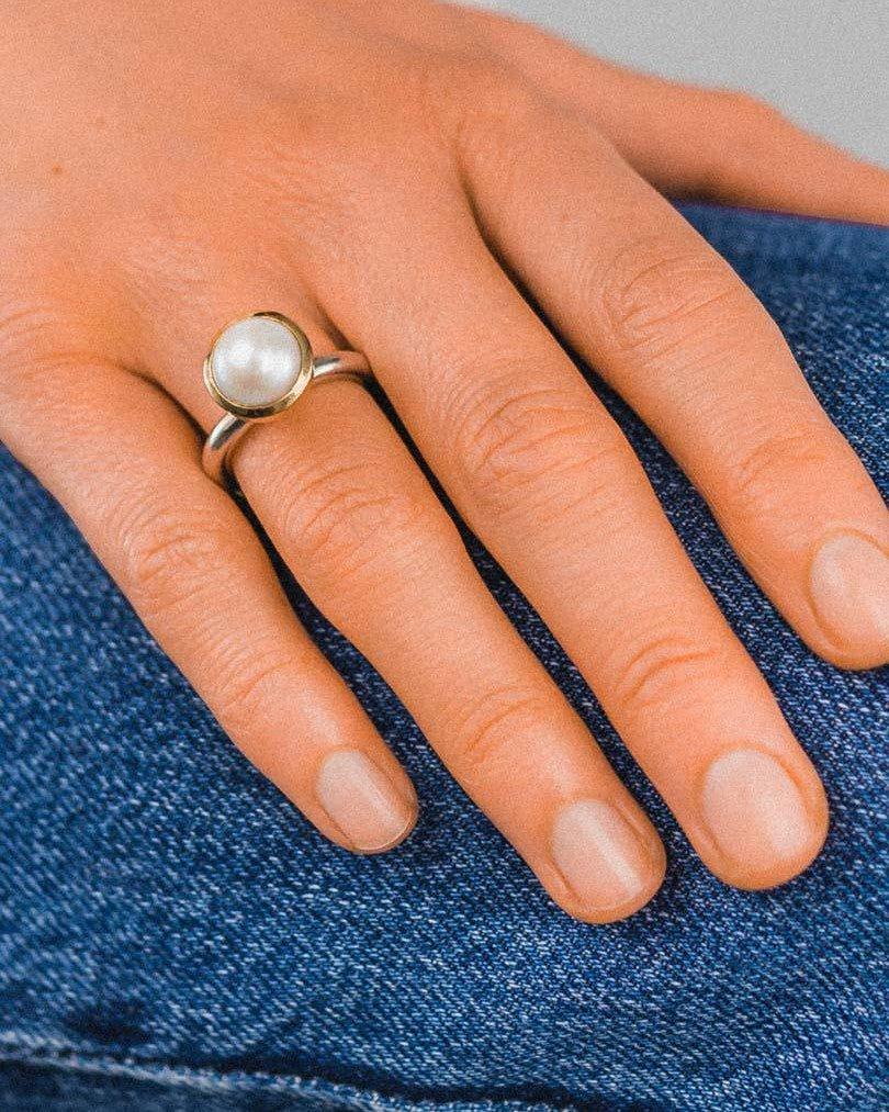 Silver and gold ring with a single white pearl on a hand.