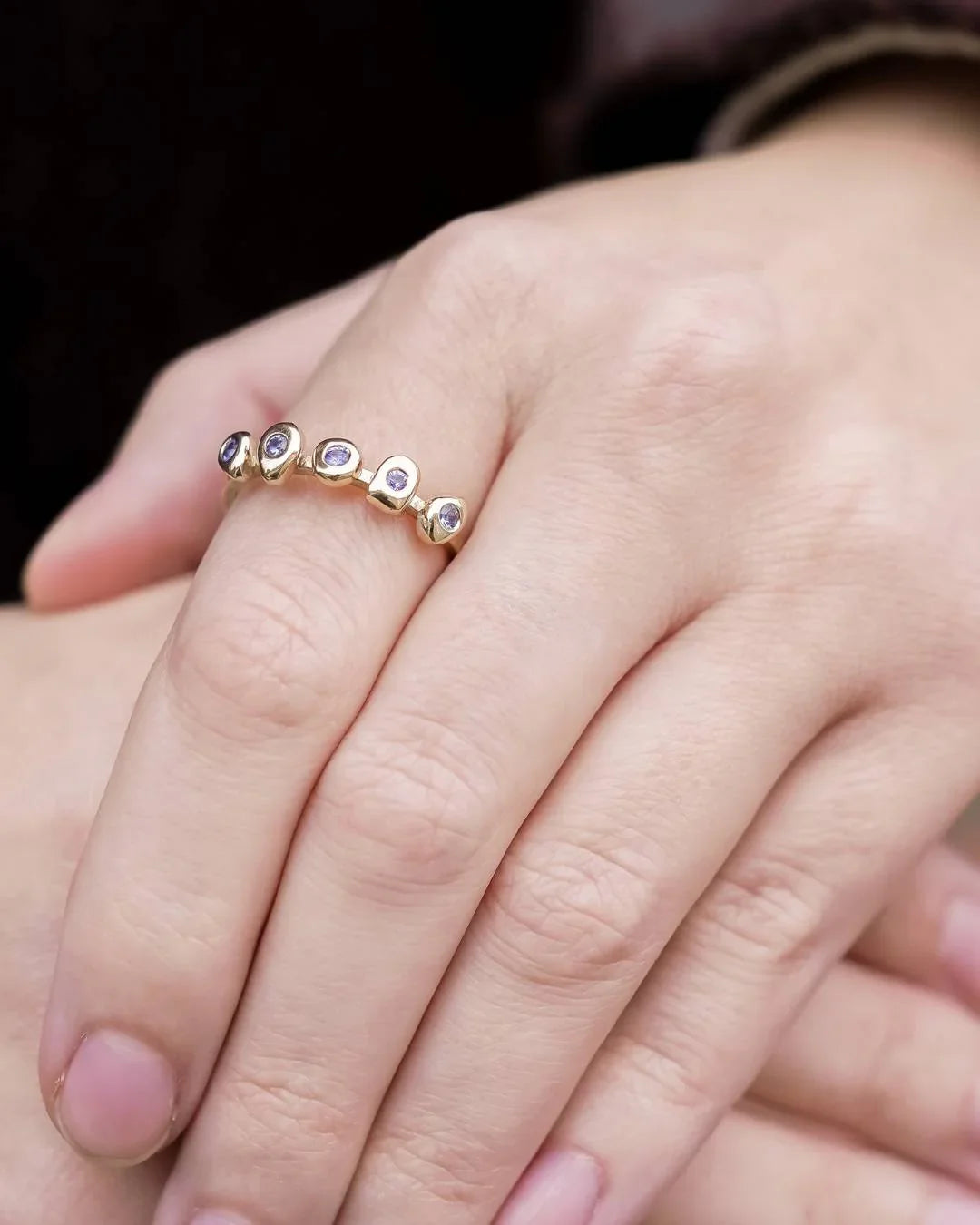 Hand wearing a unique gold ring with organic shapes and set with small purple gemstones