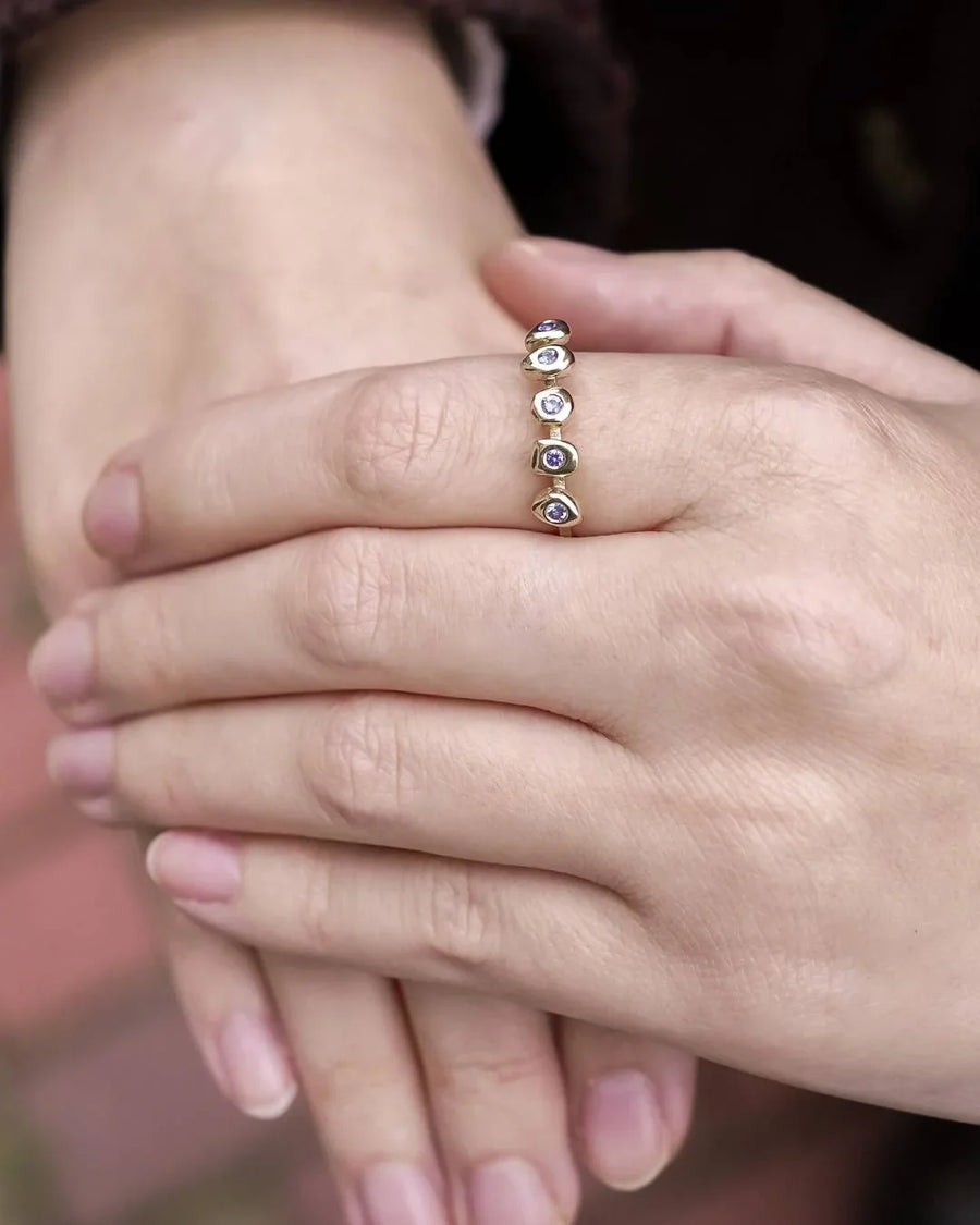 Hand wearing a gold ring with five bezel-set gemstones, handmade jewellery design