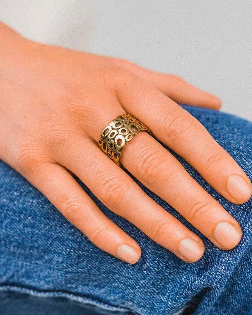 Gold pebble wedding ring with an openwork design on a hand.