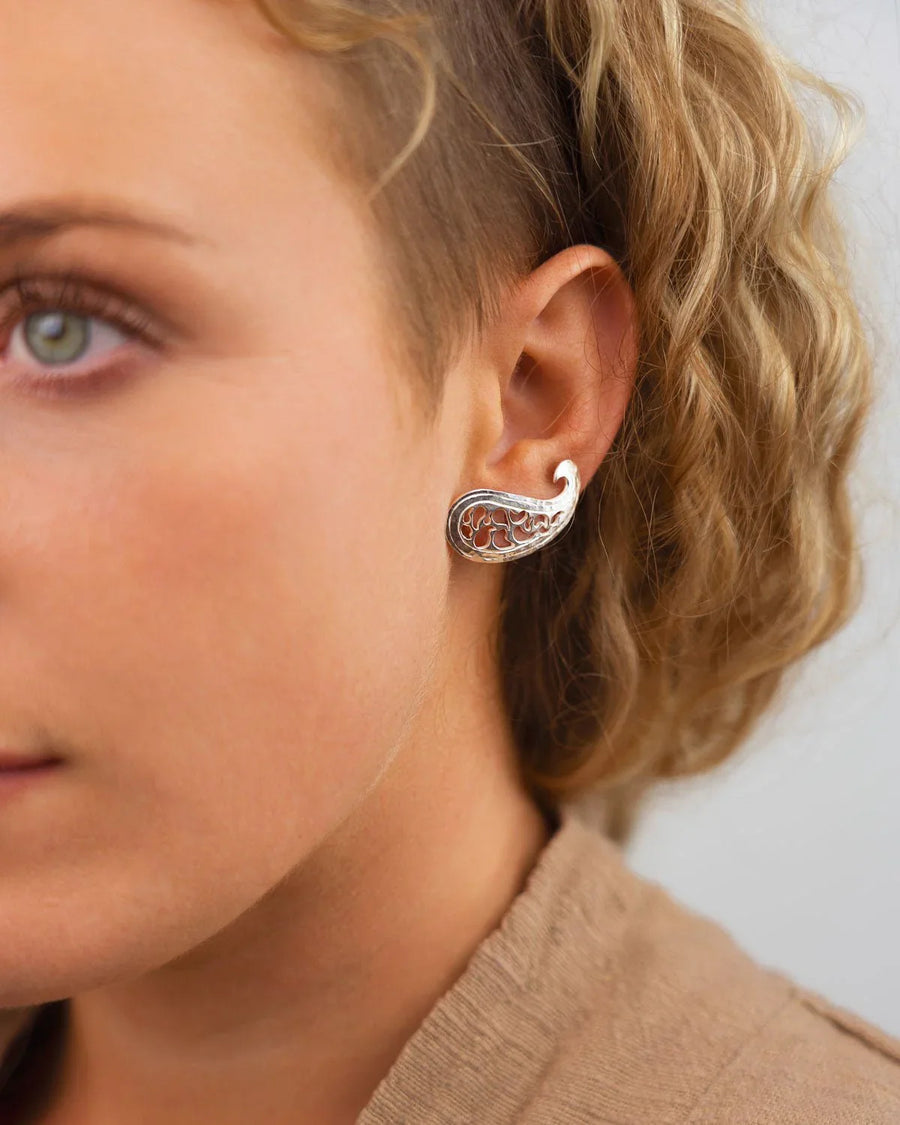 Woman wearing a silver paisley stud earring with intricate pierced design