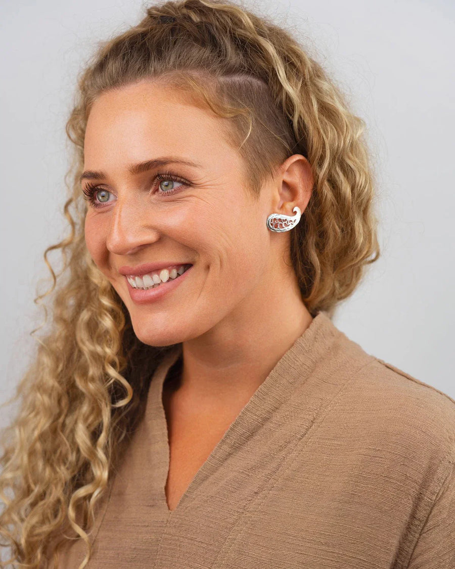 Woman wearing silver paisley stud earrings with pierced detail, smiling against a neutral background