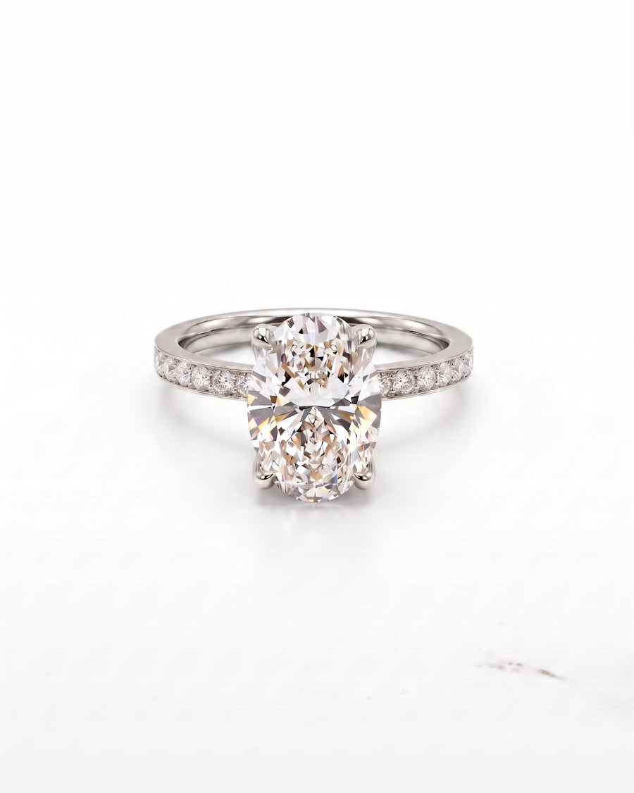 An oval-cut diamond engagement ring with a platinum band set with small pavé diamonds, photographed on a clean white background.