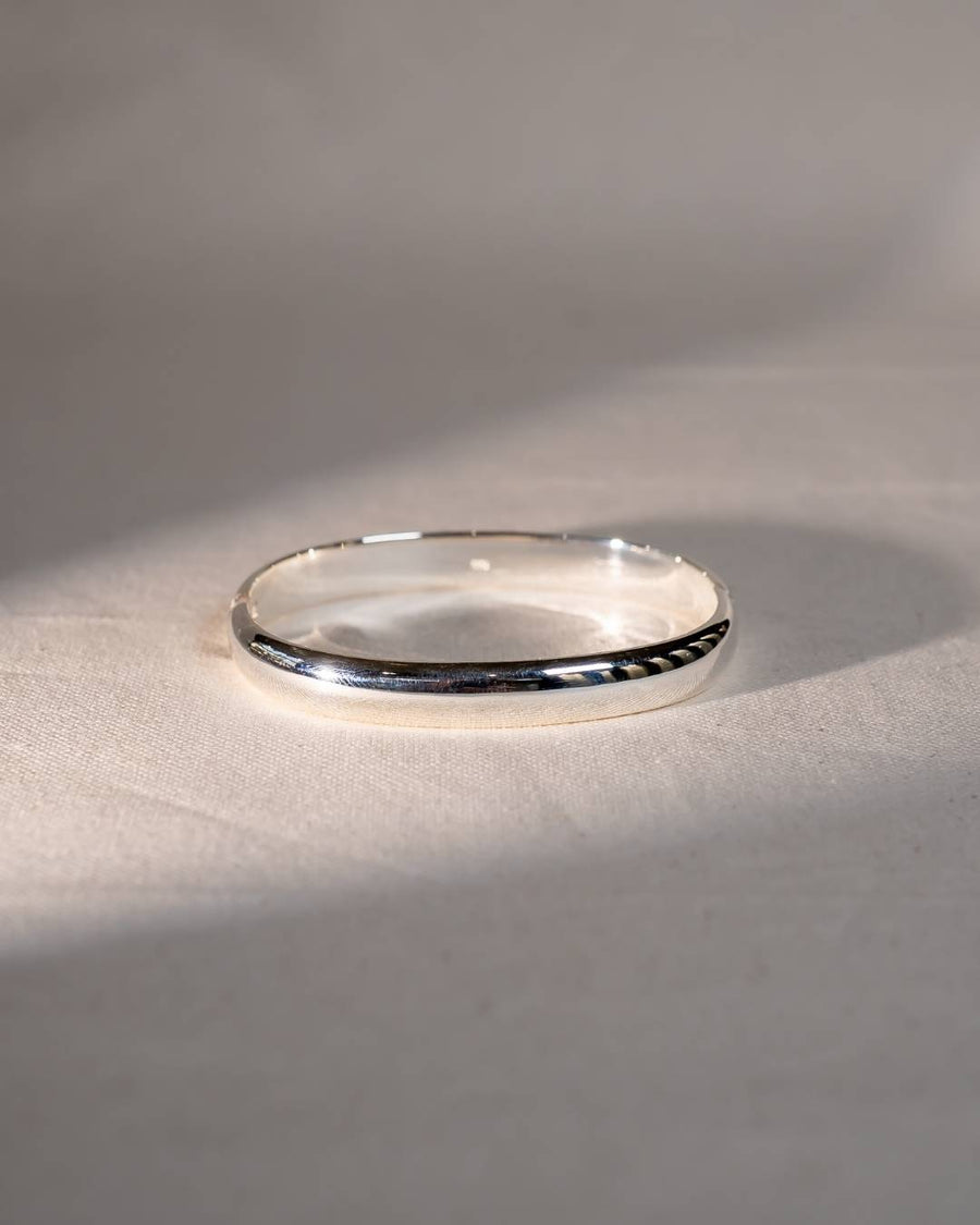Handmade silver bangle with a polished finish on a neutral fabric background