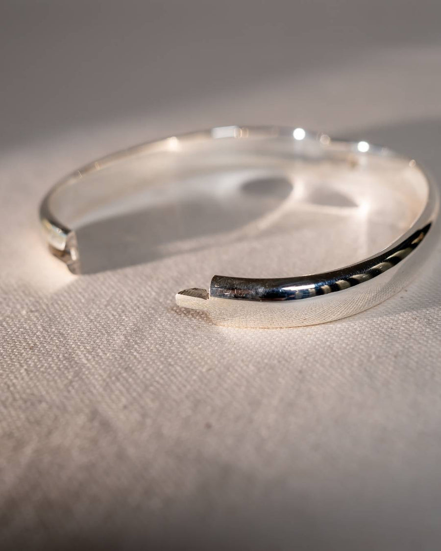 Handmade silver cuff bracelet with organic shape on textured fabric background
