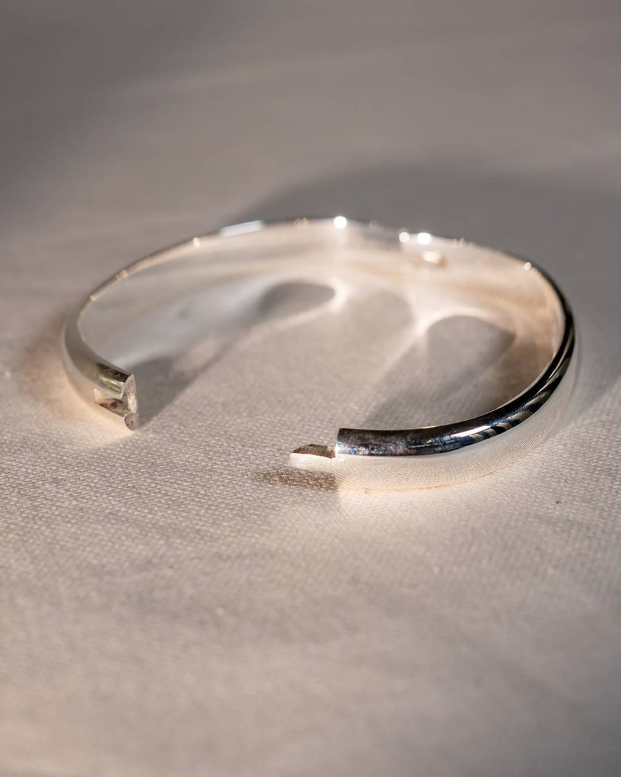 Handmade silver open bangle bracelet with a modern, minimalist design on a textured surface